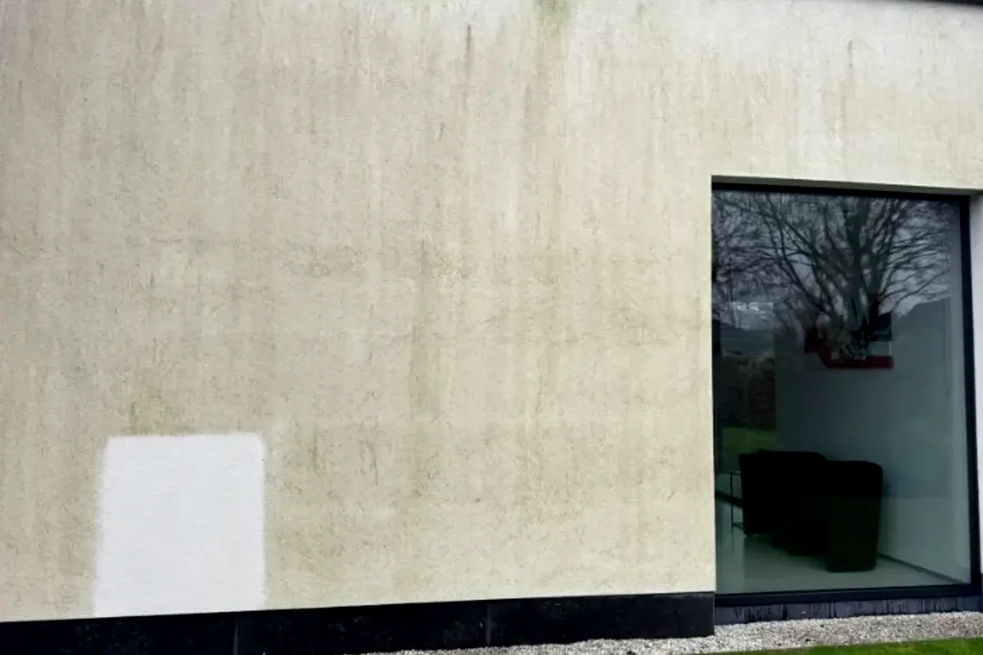 Crepigevel met groengrijze aanslag over het hele vlak; links op de muur is een klein stuk al gereinigd.