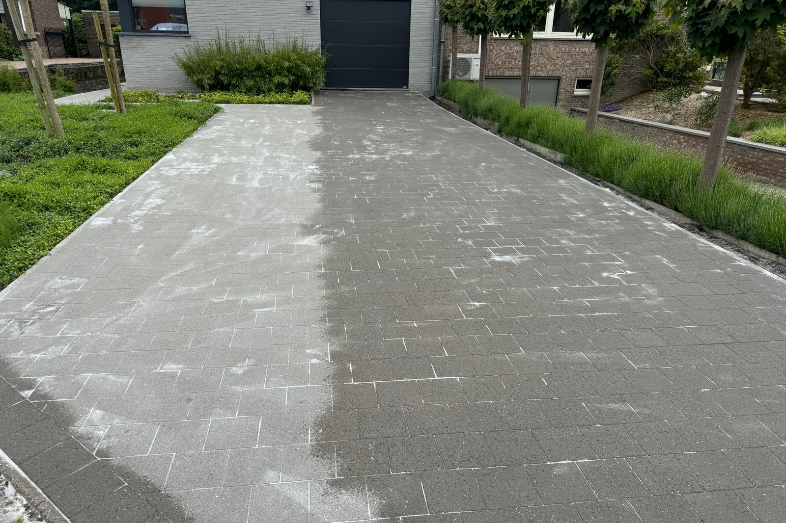 Net gereinigde oprit in grijze betonklinkers, met het voegzand zichtbaar over de bestrating en in de voegen.